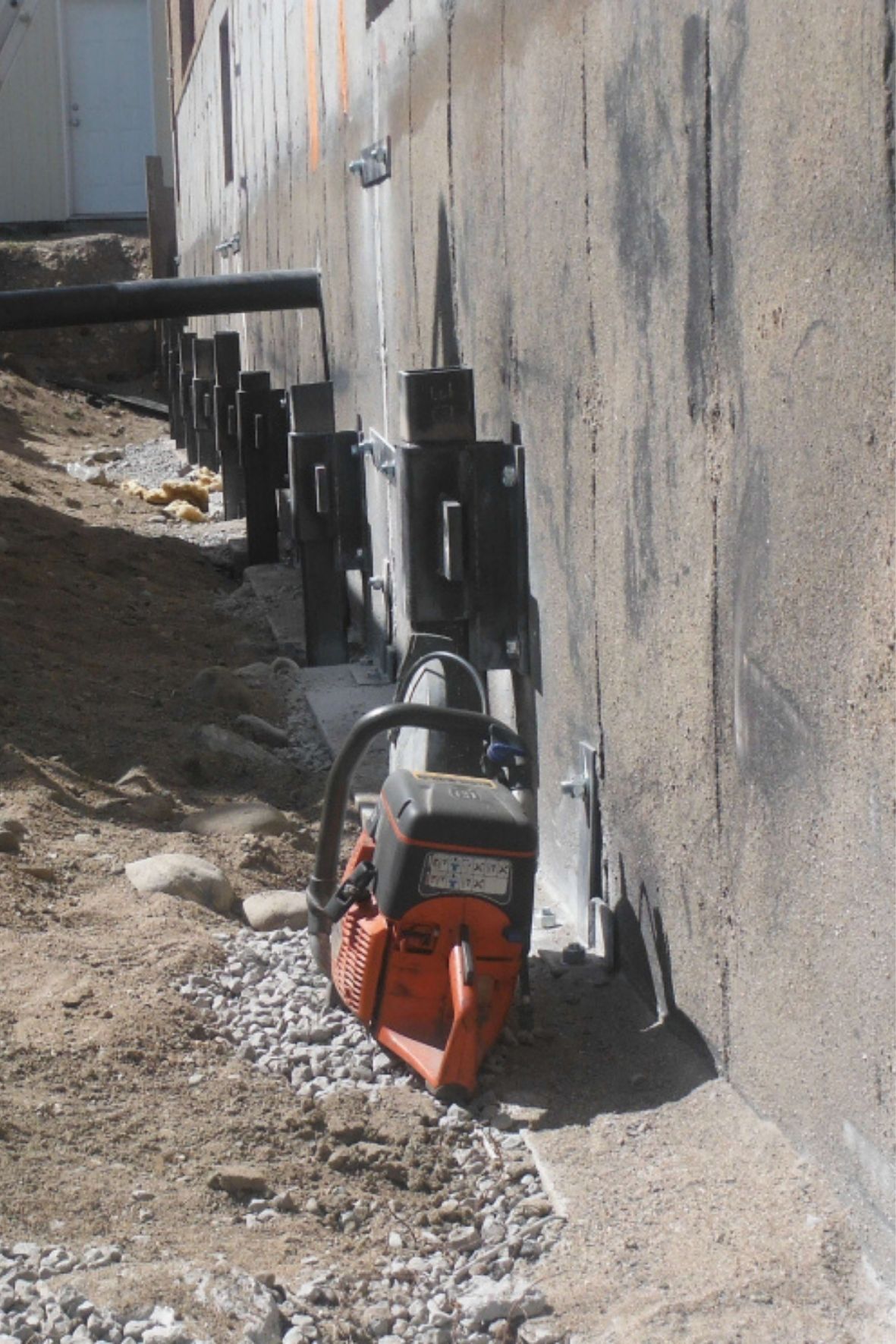 Alignement d’éléments métalliques fixés contre un mur de fondation dans un environnement de chantier  à Terrasse-Vaudreuil